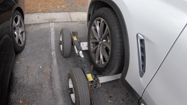 A white BMW SUV with its front left wheel loaded on a tow dolly.
