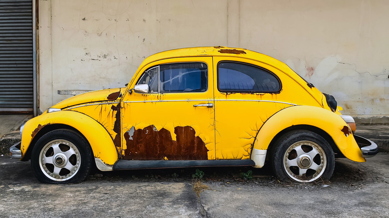 A side profile view of an abandoned yellow VW Beetle parked oh the side of the road.