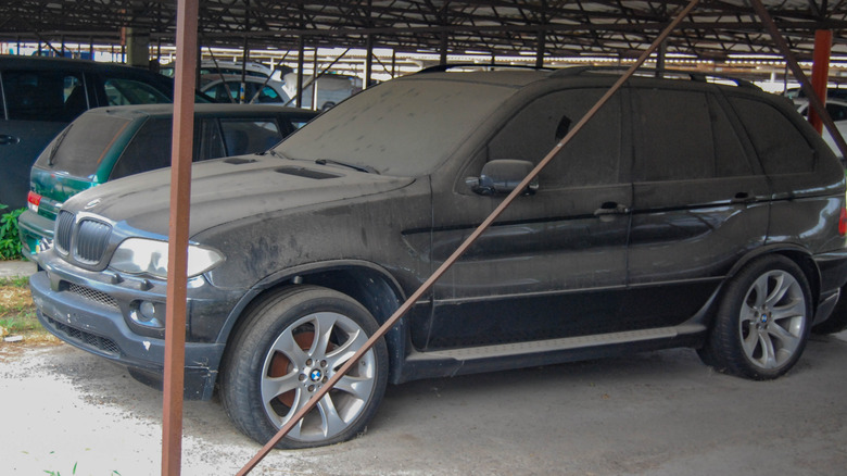 An abandoned black BMW X5 covered in dust with flat tires.