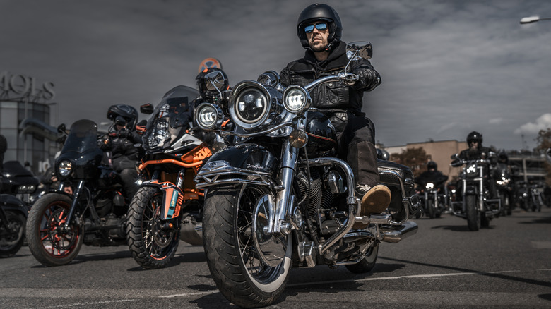 A group of bikers dressed in black ride down a street with clouds in the background
