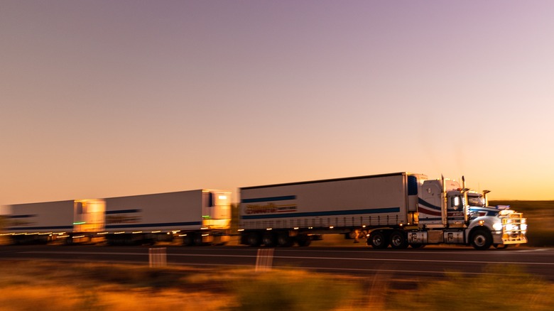 Road train travelling along a desert road at dusk