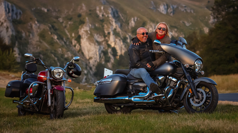 Happy middle-aged couple enjoying a motorcycle ride in the mountains. Man and woman sitting on cruiser bike, smiling and embracing, symbolizing freedom, love, travel, and adventure