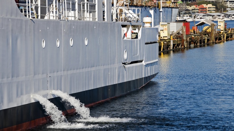 Gray docked ship at a harbor, pouring out water from its ballast tanks