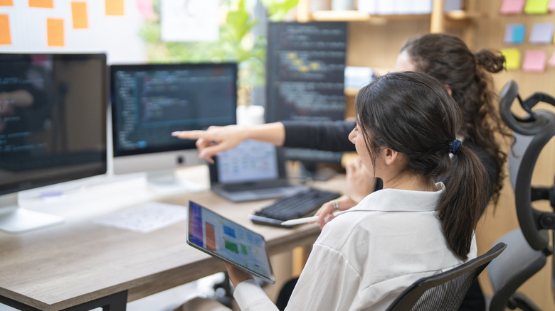 Two professionals collaborate in a modern office environment using several computer displays.