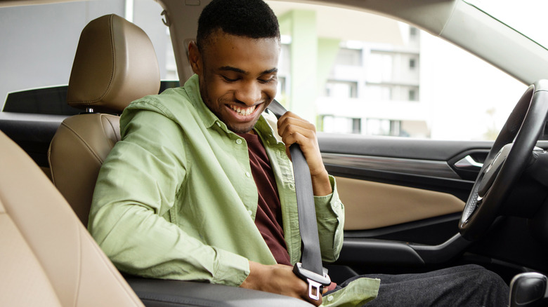 A man in a car's driver seat adjusts his seat belt.
