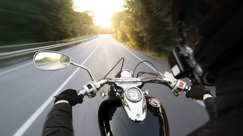 The motorcyclist is riding through the empty asphalt road in the evening