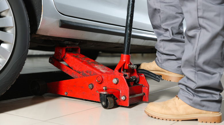 Mechanic sliding a floor jack under a car