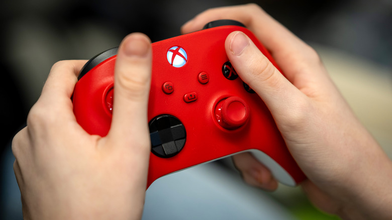 A person using a red Xbox controller with black face buttons, black D-pad and red analog sticks