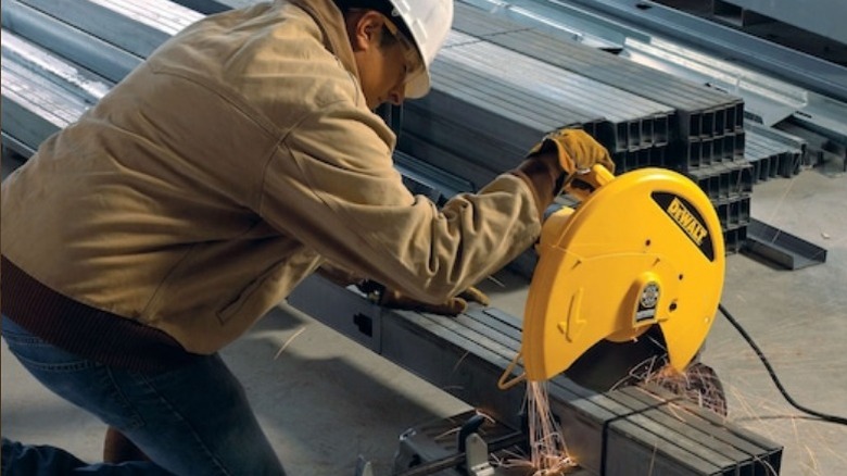 Worker using chop saw to cut metal beam