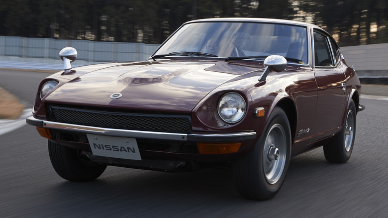 A maroon 1977 Nissan Fairlady Z driving on a racing circuit, front-view.