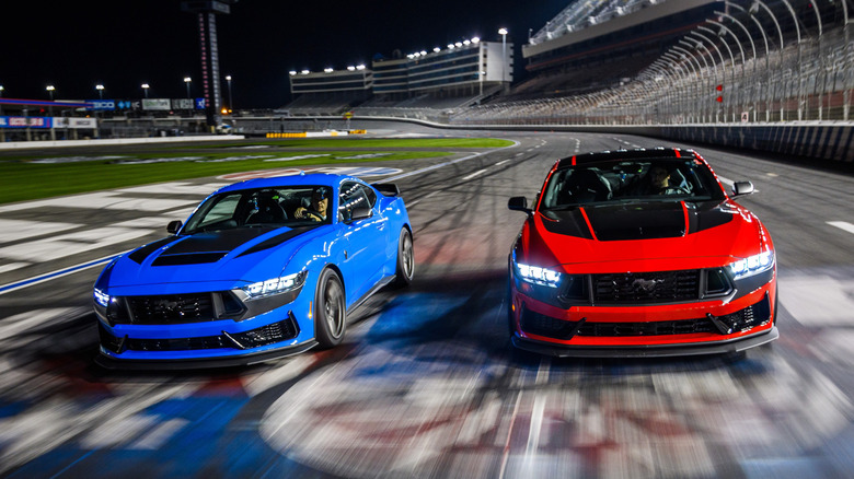 Two Dark Horse Mustangs, one red and one blue, on a race track, front view