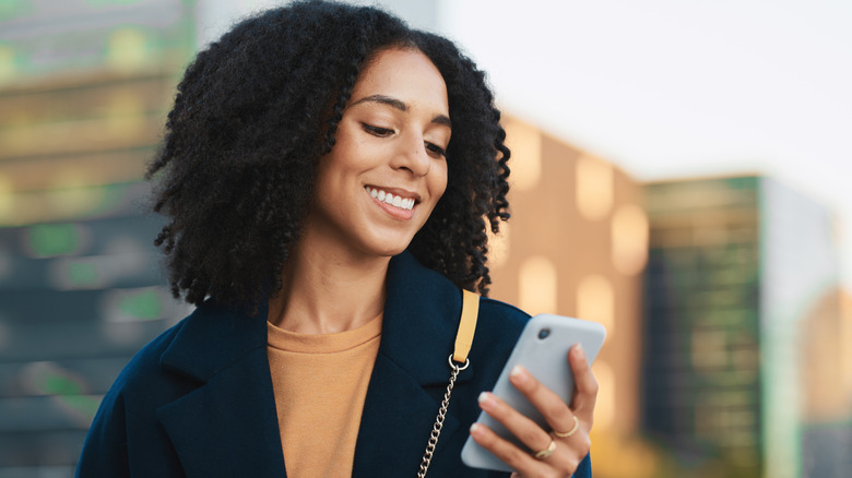 A woman smiles while looking at the smartphone in her bejeweled left hand.