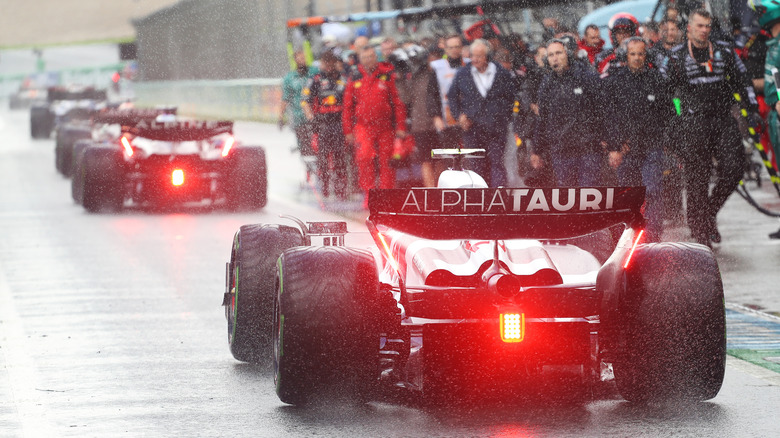 Formula One cars lined up in pit lane in rain with red rear lights lit