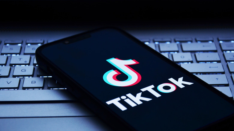 The TikTok logo is displayed on a smartphone placed above a laptop keyboard.