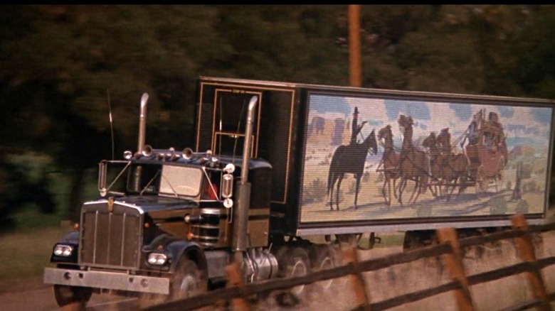 Hero shot of 1973/1974 Kenworth W900A with trailer, front-left three-quarter view, driving on road with fence in the foreground, in the film 