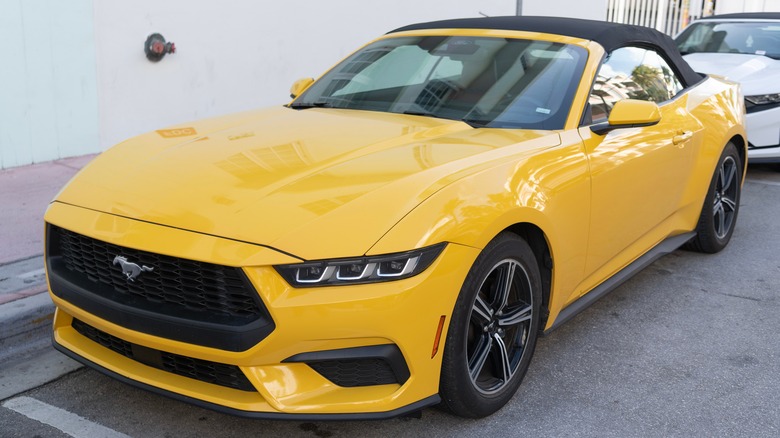 Yellow seventh-gen Ford Mustang EcoBoost convertible parked on a paved surface next to a building