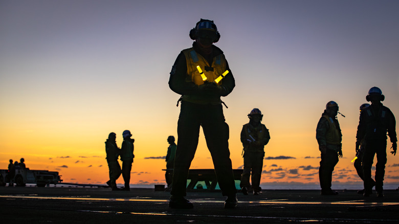 Multiple crew members on the flight deck of an American aircraft carrier at dusk