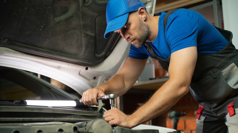 A man working on a car engine under an open hood