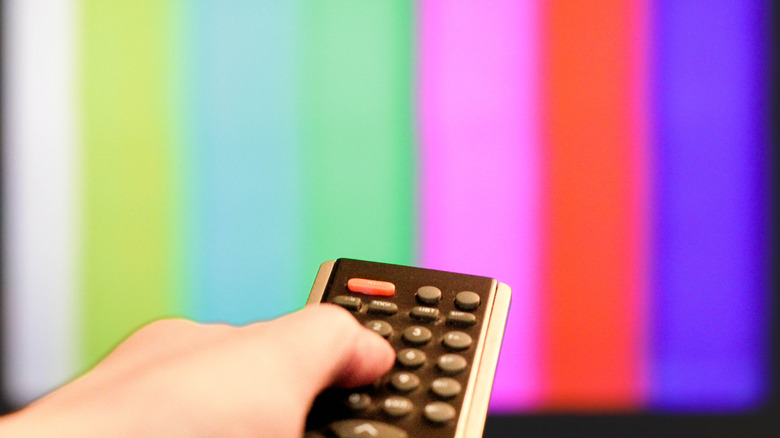 Person using a remote control on TV with color bars
