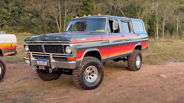 A Ford F-100 with an enclosed cab, gray with gradient stripes and M/T tires, front 3/4 view