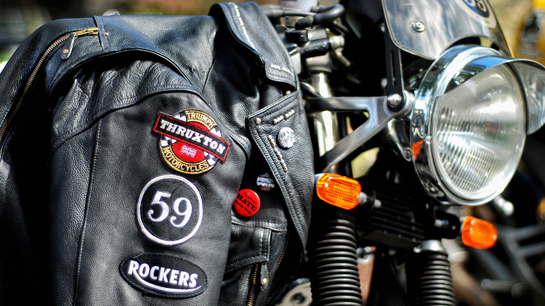 A leather jacket with patches draped over a classic Norton cafe racer motorcycle.