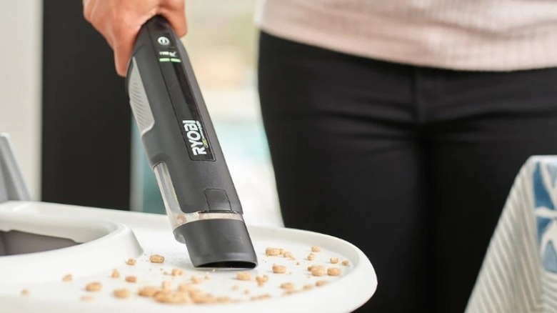 Person holding vacuum cleaning food off a high chair tray