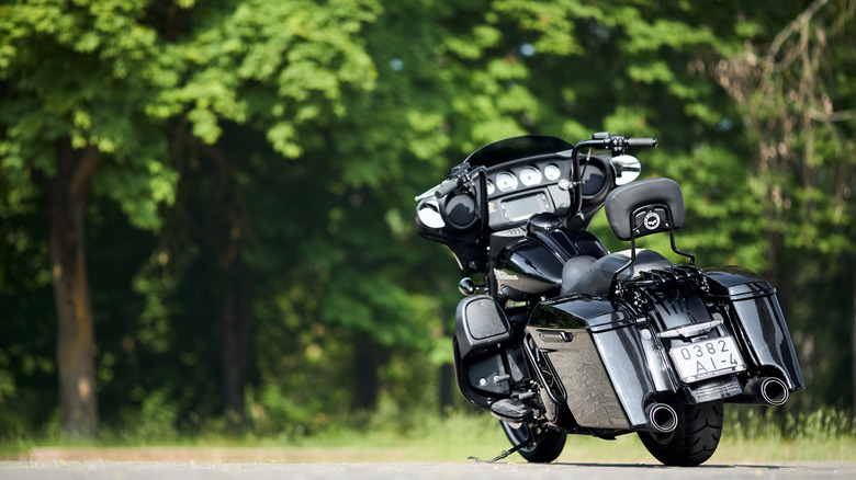 The rear of a black Harley-Davidson HD Street Glide parked next to the road with bushes in the background