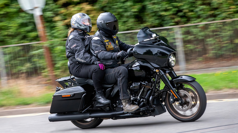 Two people riding a 2023 black Harley Davidson Street Glide motorcycle travelling on a British road