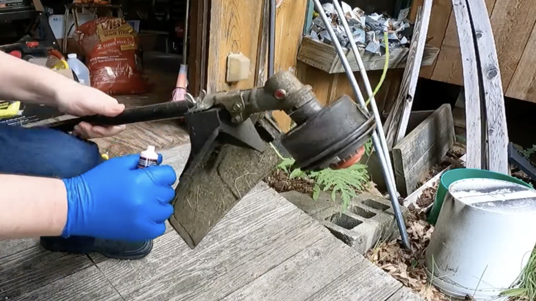 Man in blue gloves greasing a string trimmer