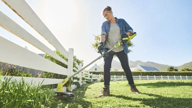 Woman using Ryobi string trimmer along white slatted fence