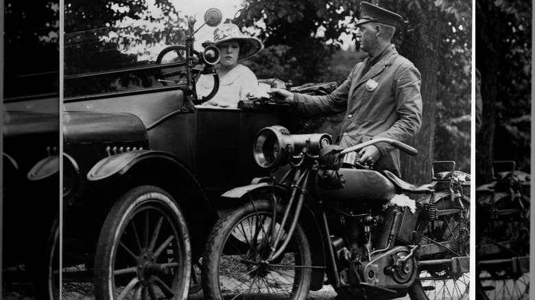 Motorcycle policeman in Washington giving woman ticket for travelling 25 miles per hour, which is in excess of the 18 miles per hour allowed by law.