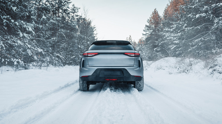 A rear-end view of a silver SUV positioned in the middle of a snowy road with trees in the background.