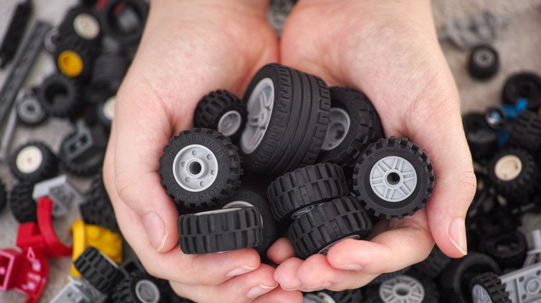 A young boy holding a handful of Lego wheels in his hands.