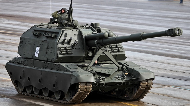 A Russian 2S19M2 Msta-S self-propelled howitzer during a Victory Day parade with a soldier saluting from an open hatch/