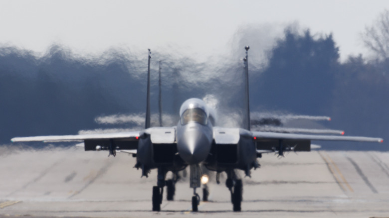 A trio of F-15s taxi on a runway with heat plumes coming off the lead jet