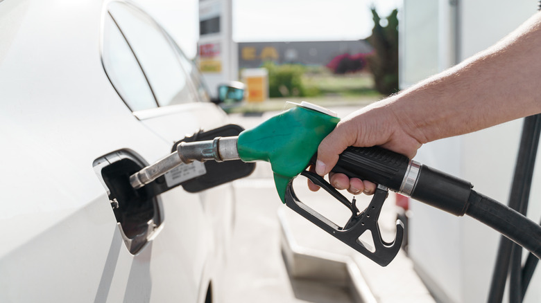 A man's hand holding green gas pump while refueling car with diesel oil.