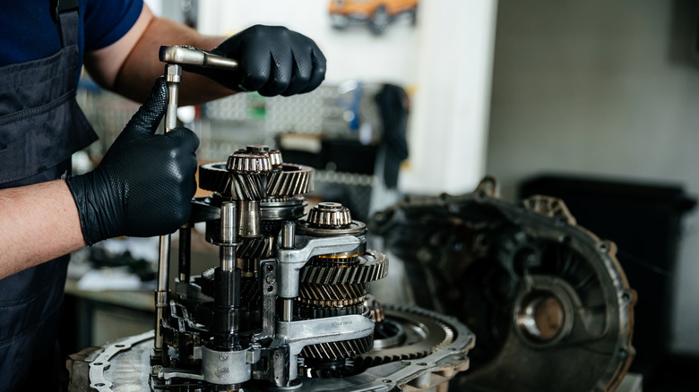 A mechanic's gloved hands holding tools while repairing a manual gearbox at a service station