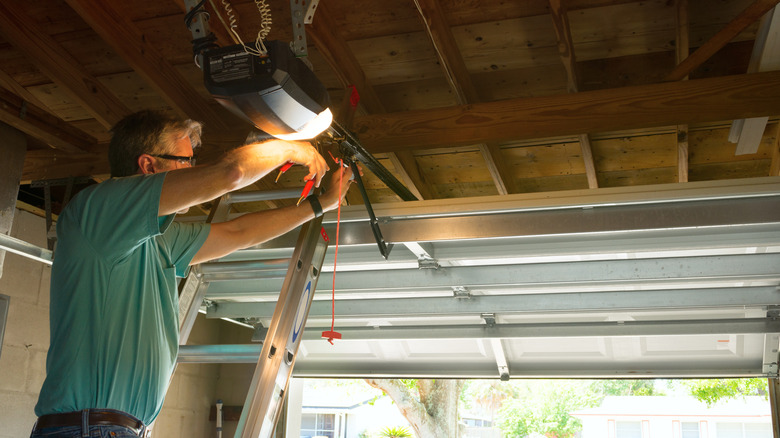 A person installing a garage door mechanism on a stepladder