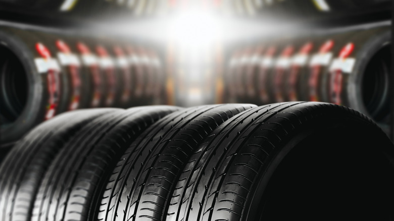 Four passenger car tires in the foreground, with an out-of-focus tire shop in the background
