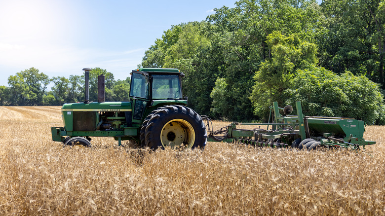 A John Deere tractor with a harvester trailer in a wheat field, side view