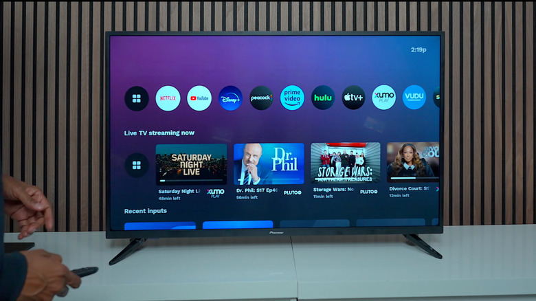 A person holding a remote next to a 4K Pioneer TV, several apps and live TV channels shown