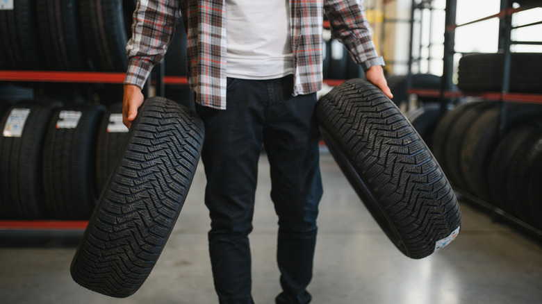A person carrying two brand new tires through a tire shop.