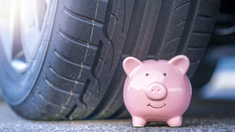A small pink toy pig positioned in front of a car tire, symbolizing savings.
