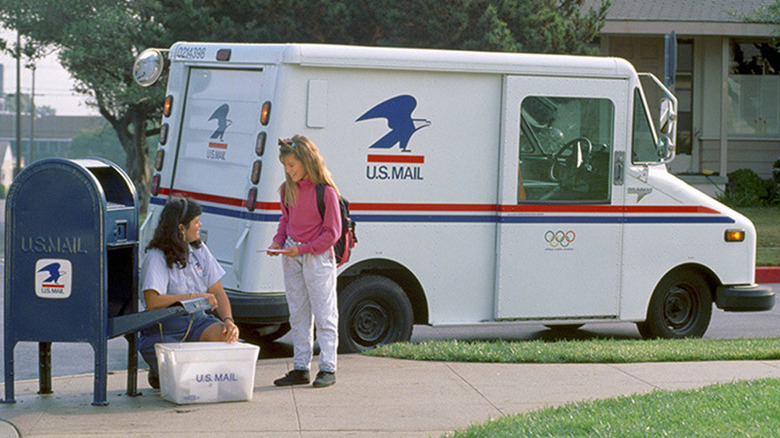 Rear 3/4 view of LLV in neighborhood setting, with young girl giving mail to mail carrier at open mail box