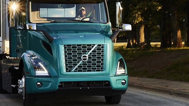 Volvo electric semi-truck driving down a road lined with trees