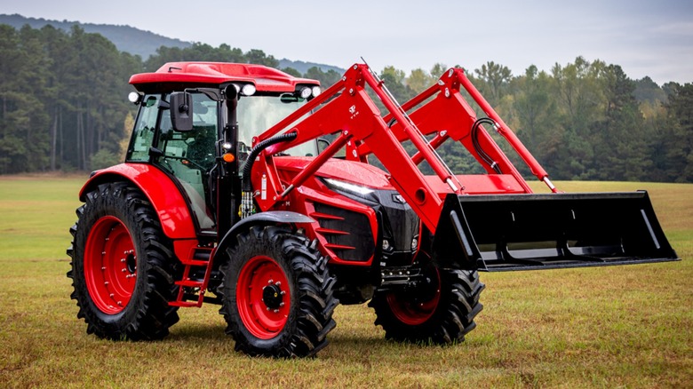 a red tym t130 tractor sitting in a field with woods in the background