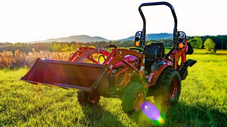 a red tym t224 tractor sitting in a field with mountains in the background