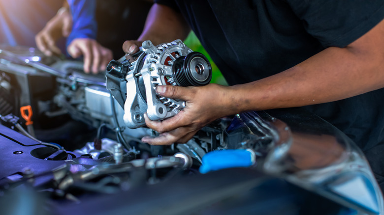 A mechanic holding an alternator over a car's engine bay.