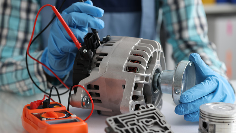 A person in gloves testing out a car alternator with a multimeter.