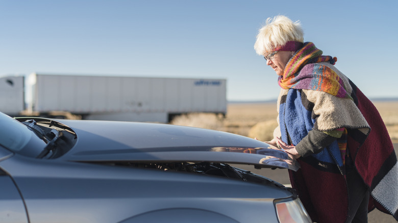 Elderly lady lifting the hood of a car
